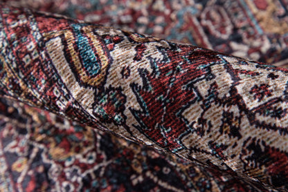 Rolled Persian-style rug with red, ivory & teal floral patterns and dense oriental motifs.