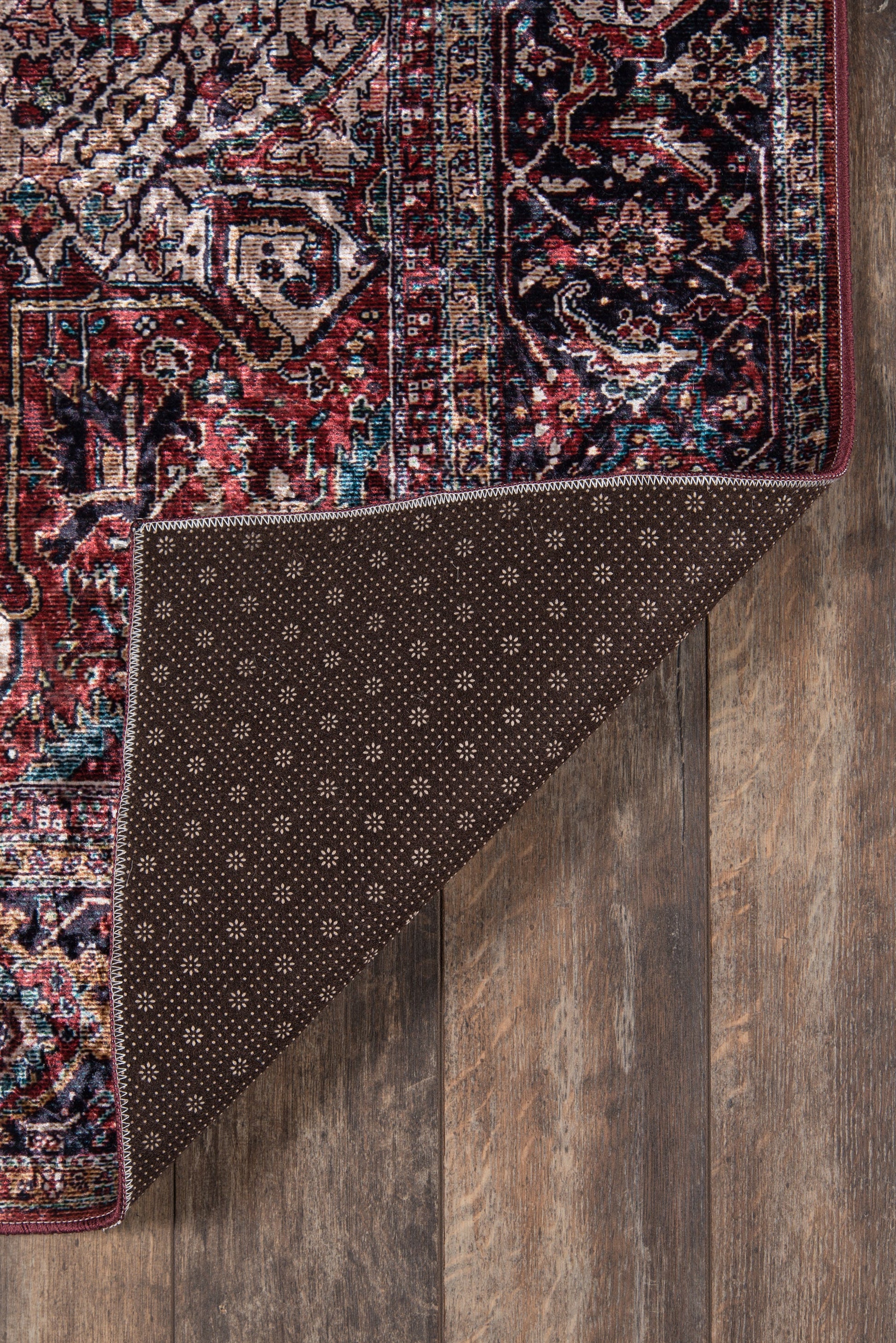 Karackar rug, rectangular, with red, blue, ivory Persian pattern; folded corner reveals brown dotted backing on wood floor.