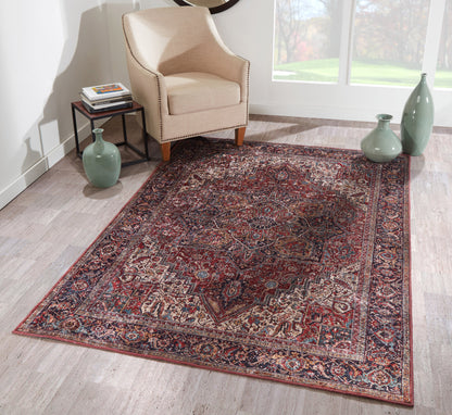 Beige armchair with nailhead trim beside a red-and-navy Persian rug on light wood floor; green vases and bright window light.