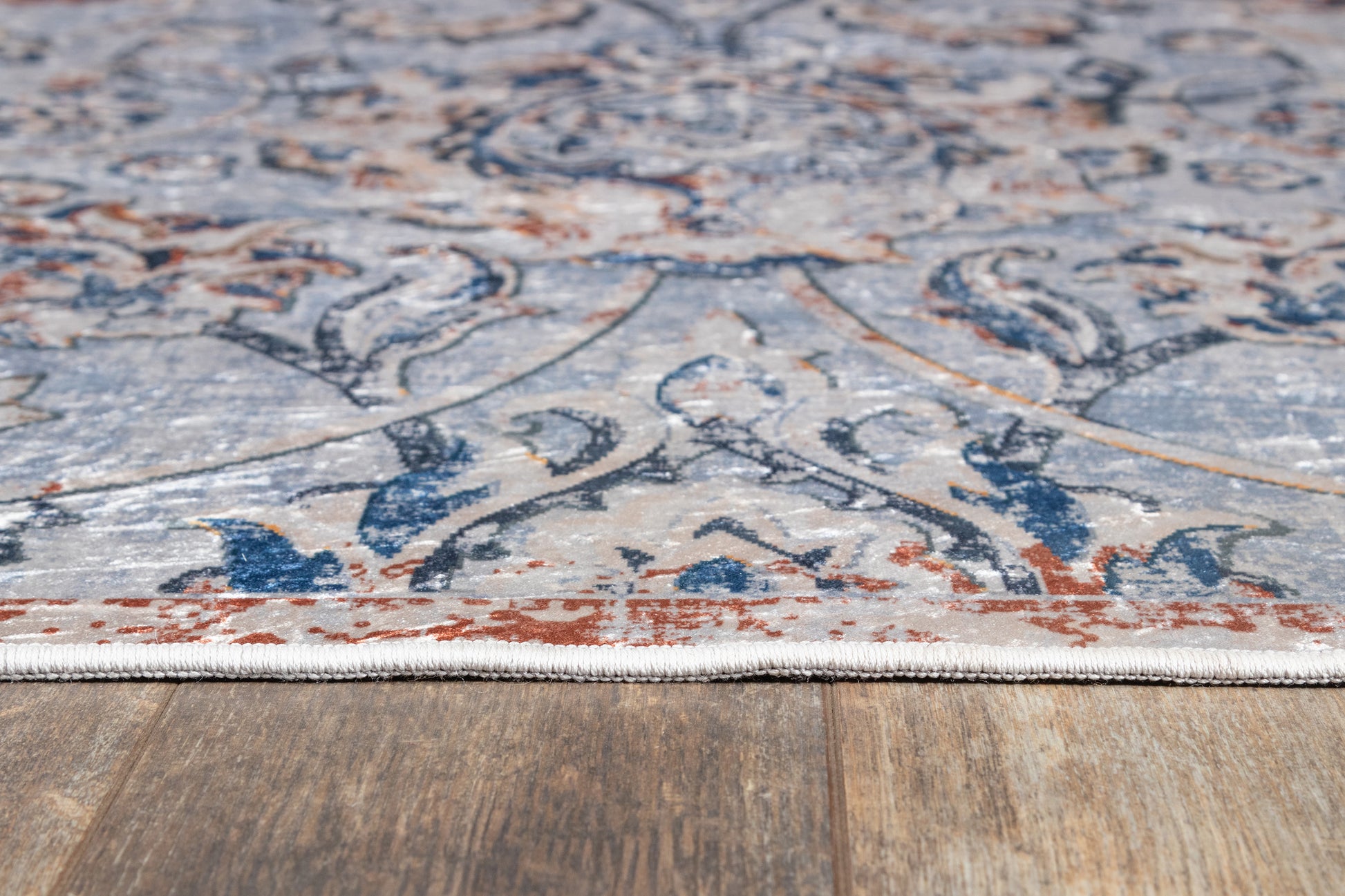 Low-angle view of a patterned rug edged with light fringe on a wood floor; blue, ivory, and rust tones in a classic oriental motif.