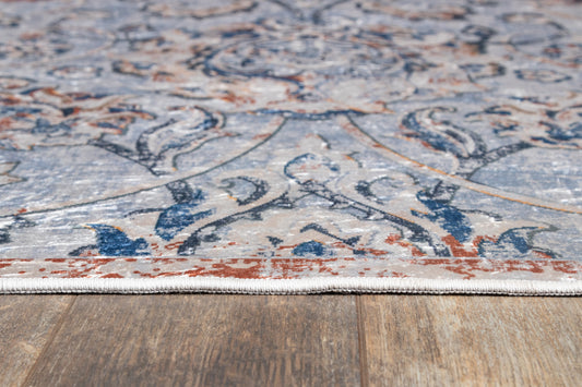 Low-angle view of a patterned rug edged with light fringe on a wood floor; blue, ivory, and rust tones in a classic oriental motif.