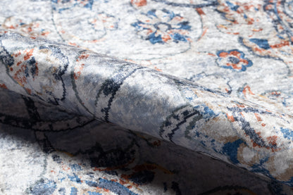 Close-up of an ornate blue-ivory rug with orange accents and floral motifs; folded edge reveals soft, textured pile.