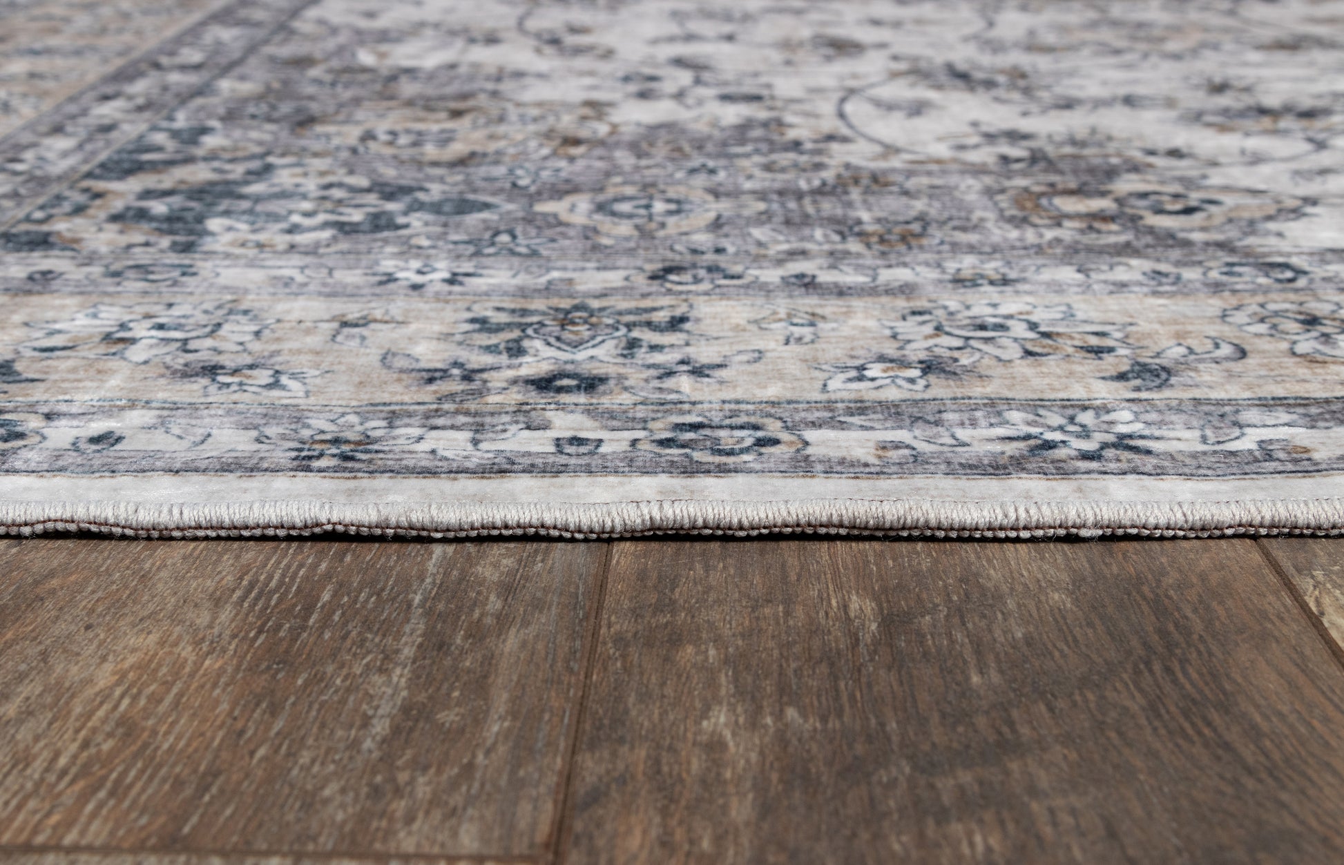 Gray and blue oriental-style area rug with floral motifs and fringe on dark wood floor