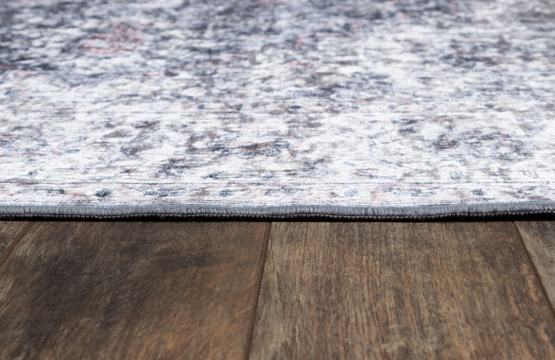 Rectangular gray-blue distressed area rug with dark binding, laid on wood floor.
