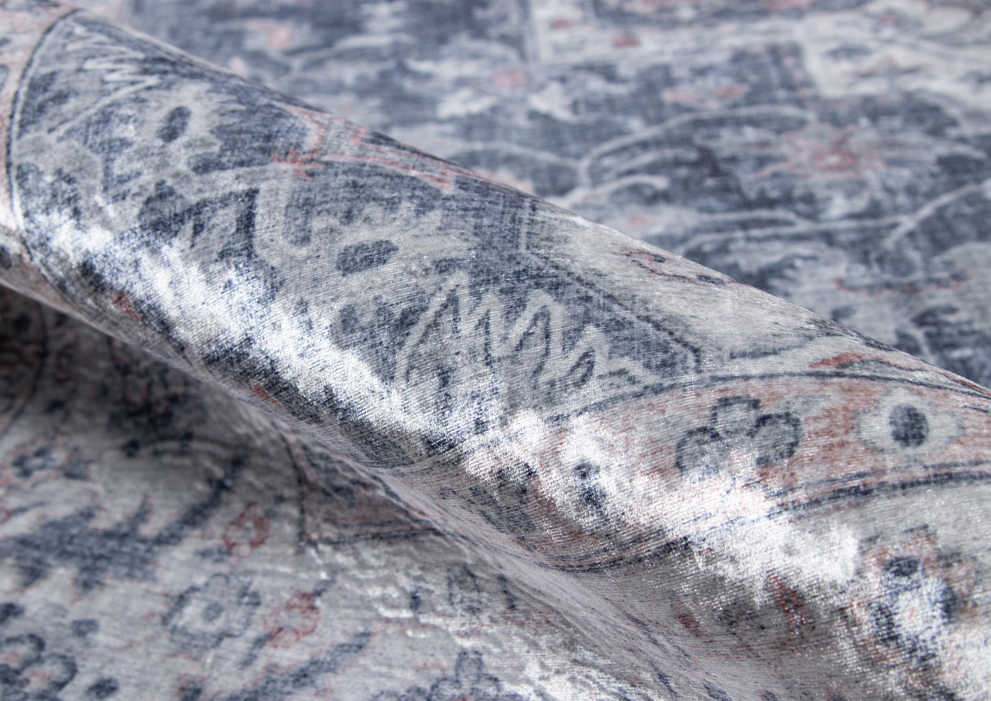 Grey-blue oriental rug with faded floral motif, rolled corner displaying soft textile.
