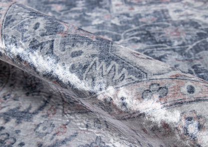 Grey-blue oriental rug with faded floral motif, rolled corner displaying soft textile.