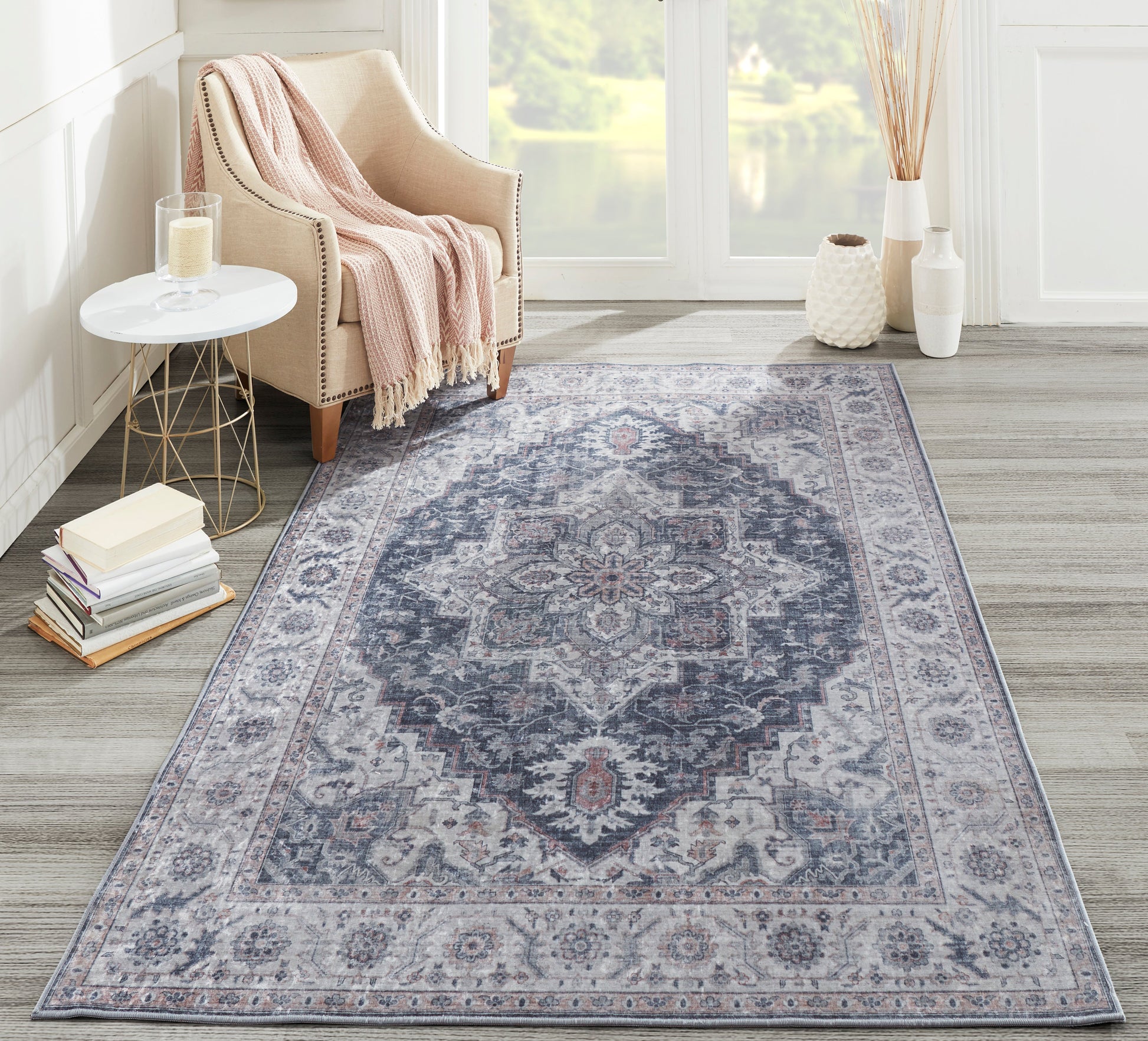 Gray-blue oriental area rug with central medallion on hardwood floor, beige armchair and pink throw in a cozy living room.