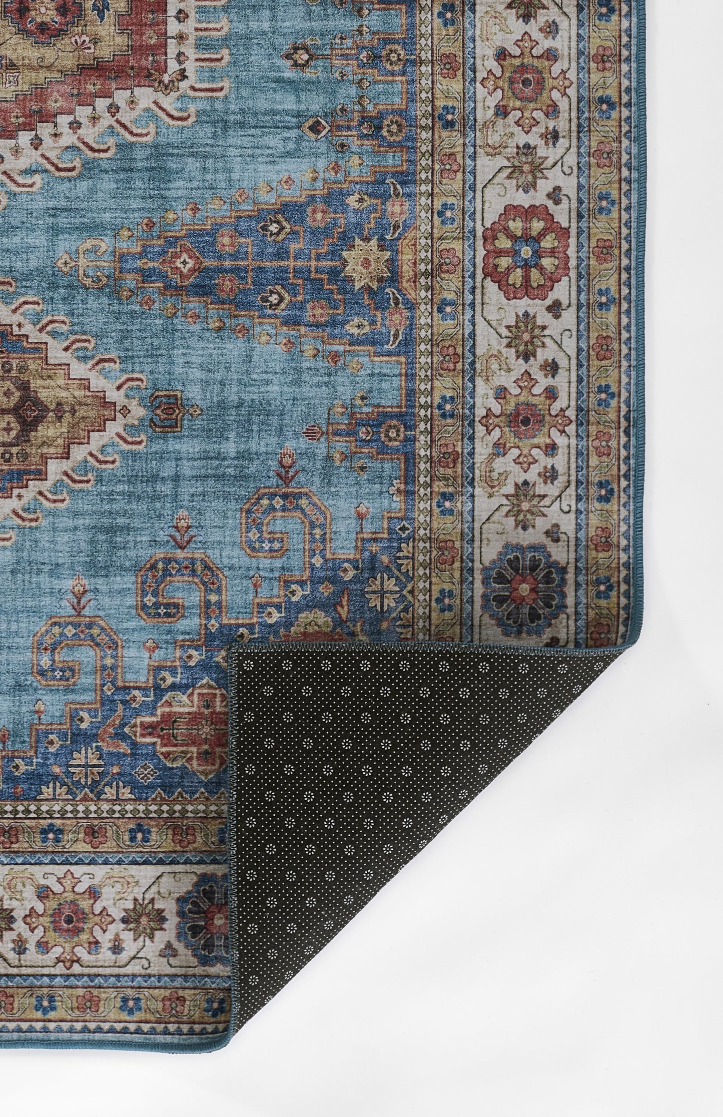 Blue oriental rug with beige borders and red accents; ornate geometric motifs, corner folded to show dark dotted backing.
