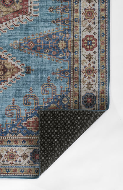 Blue oriental rug with beige borders and red accents; ornate geometric motifs, corner folded to show dark dotted backing.