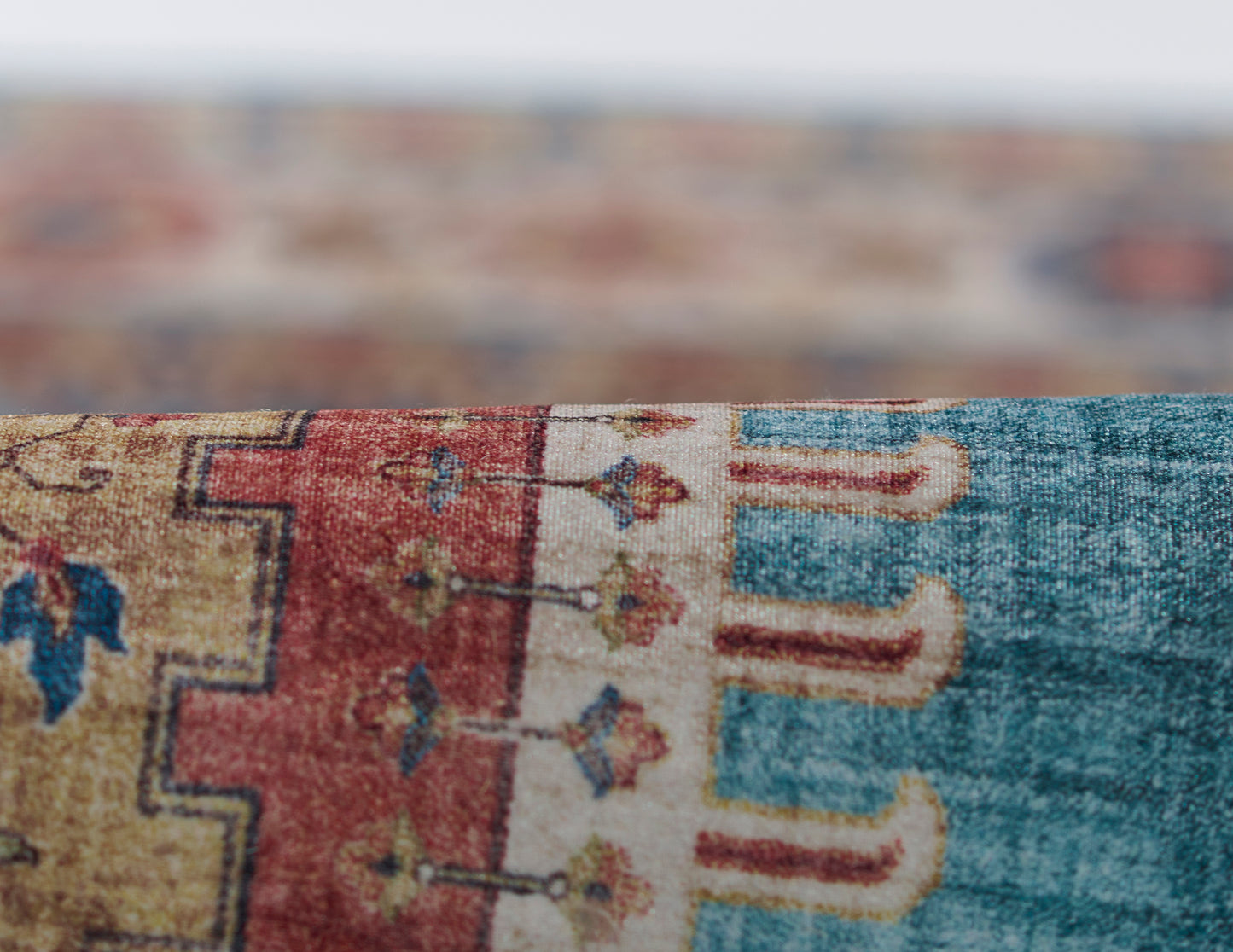 Close-up of a woven area rug with teal, red, and beige geometric motifs and a soft textured pile.
