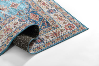 Blue oriental rug with cream and red floral border, turquoise edge, rolled corner showing dark non-slip underside.