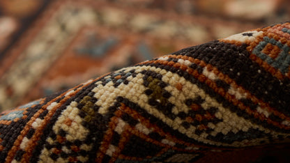 Close-up of a rolled oriental wool rug with bold geometric tribal pattern in cream, brown, blue and orange.