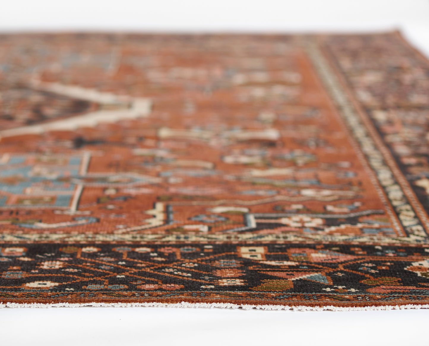 Red Karajkaj rug with intricate geometric border in navy, tan and ivory; low-angle close-up showing fringe edge.