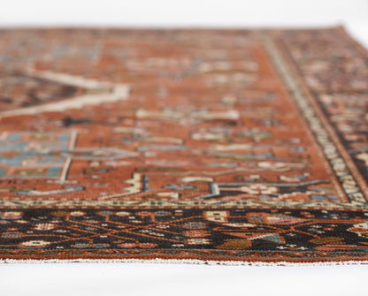 Persian-style rug with red field, dark border, blue/cream geometric motifs; woven wool, fringe along edge.