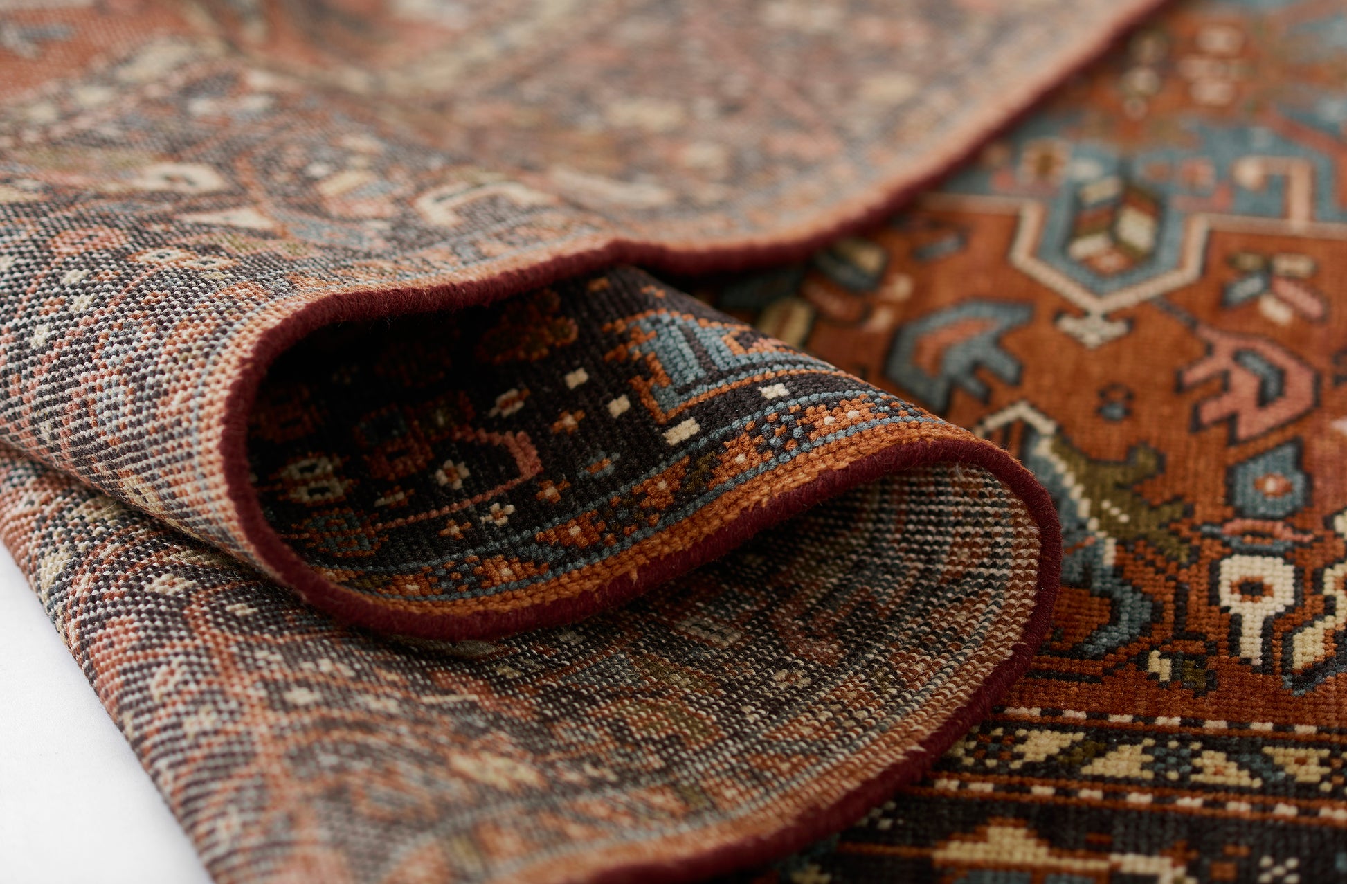 Traditional Persian-inspired rug in red, rust, blue and ivory; wool weave with geometric motifs, folded edge showing texture.