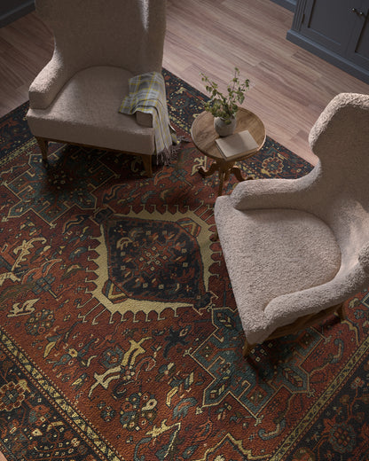 Two beige boucle armchairs surround a round wood side table with a plant on a red-blue-gold patterned oriental rug.