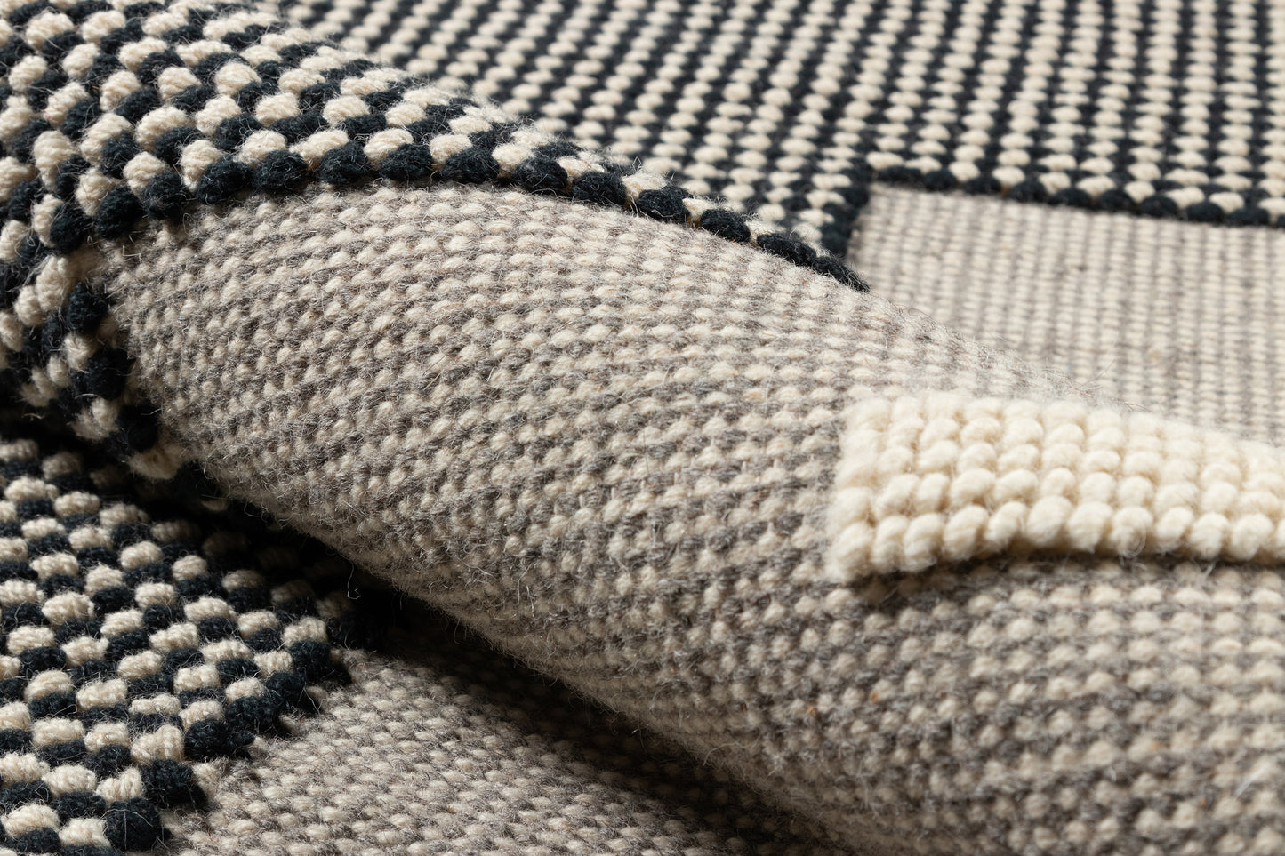 Close-up of a black and beige boucle woven throw blanket with chunky texture, folded edge.