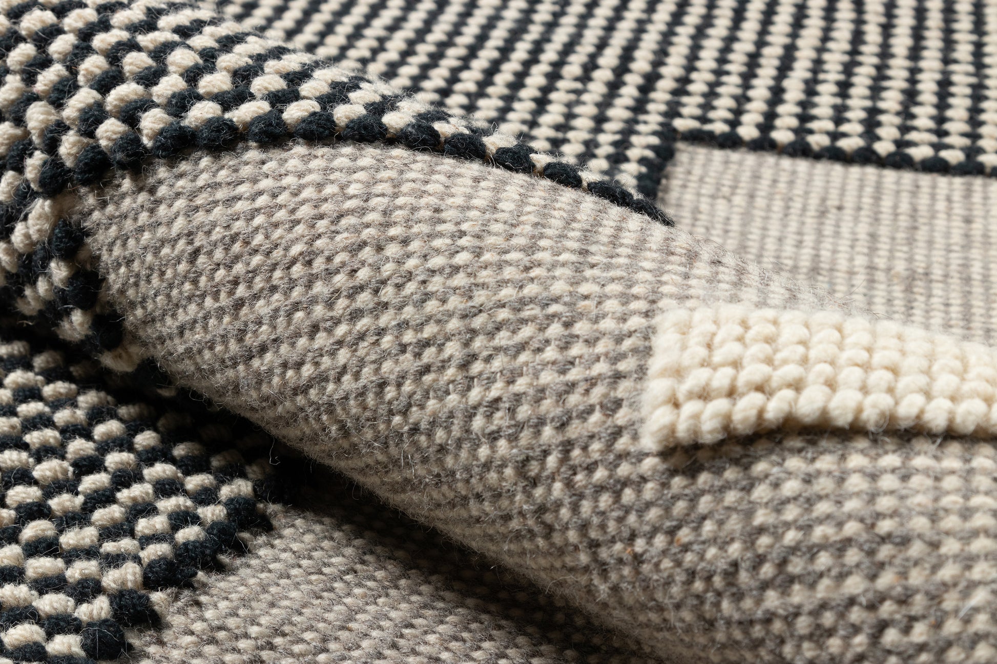 Close-up of a beige and black boucle woven throw blanket with a checkered texture and folded edge.