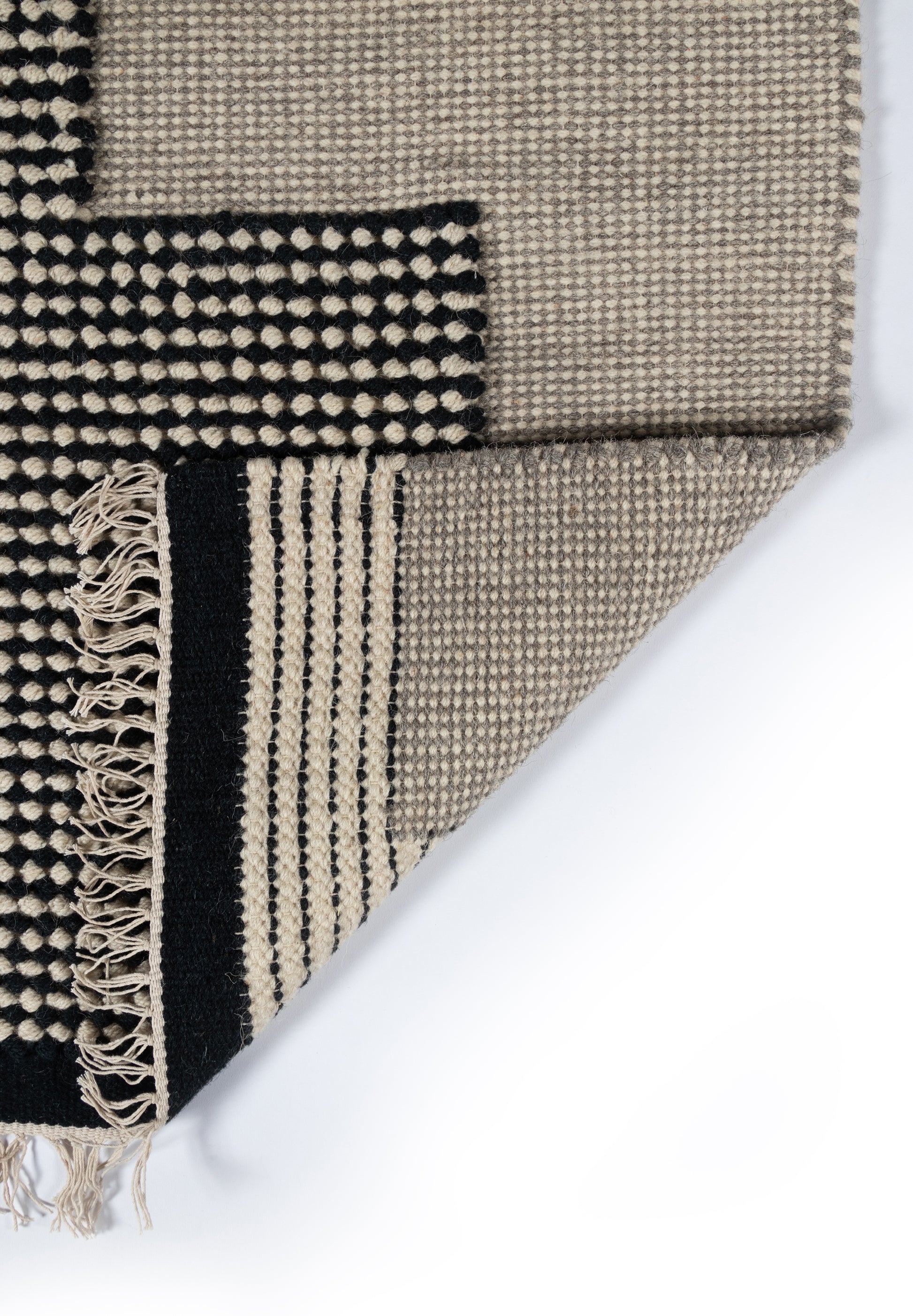 Beige and black woven rug with geometric pattern, fringed edge, layered look; wool-like texture.