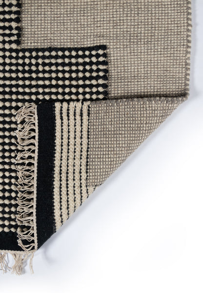 Beige and black woven rug with geometric blocks and fringed edge.