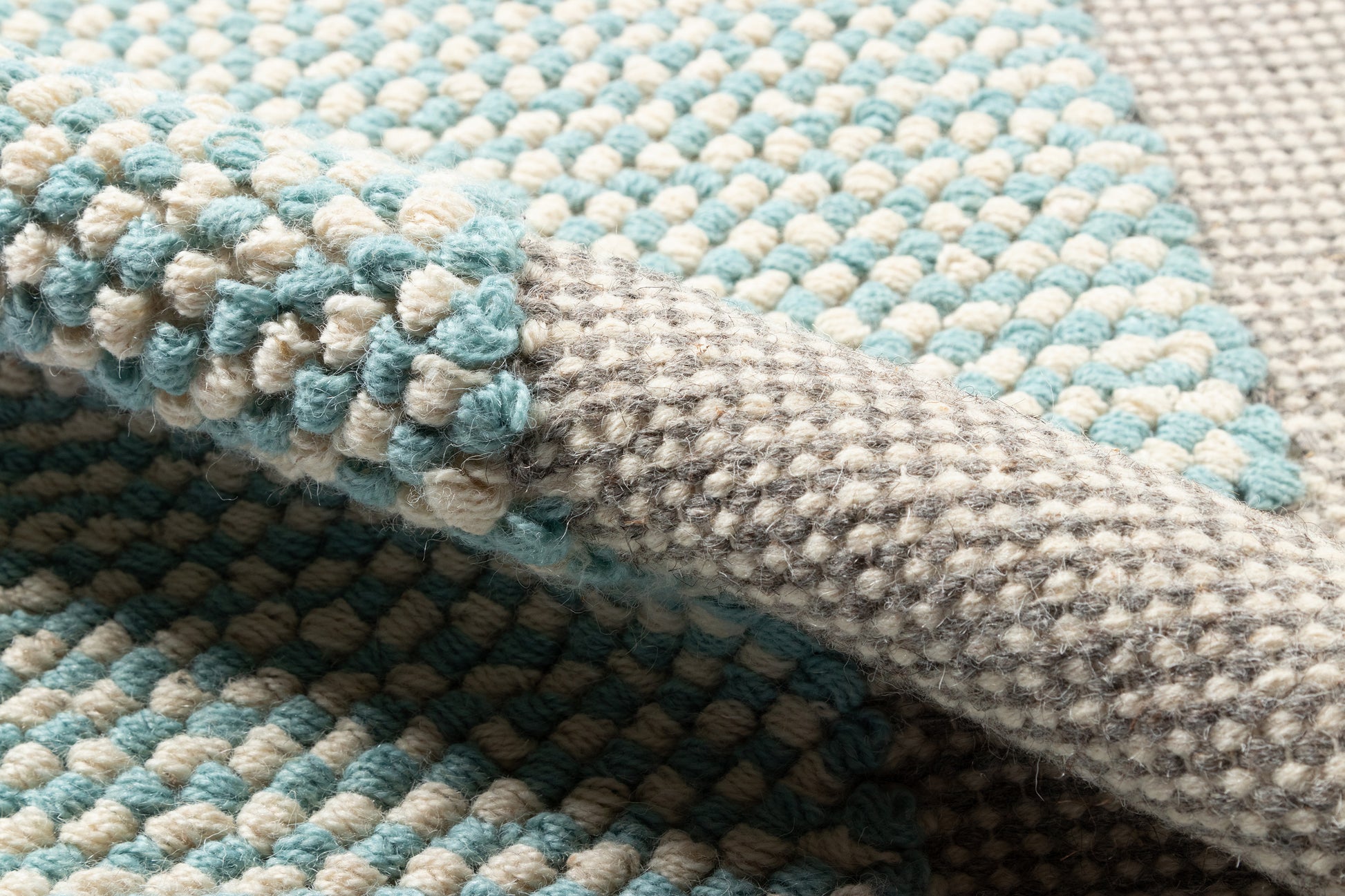 Chunky woven rug in blue teal and beige with soft loop texture and a grey folded edge.