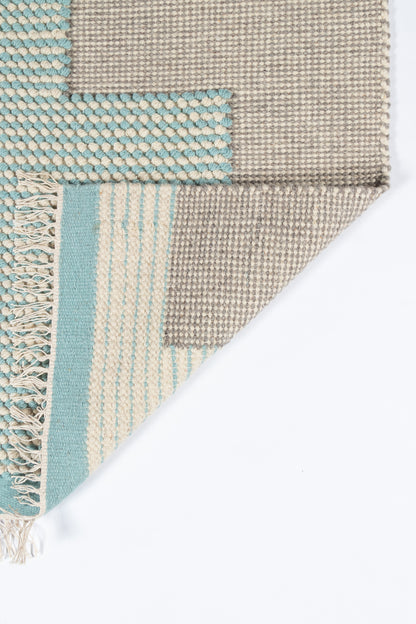 Beige and aqua patchwork woven rug with fringe; natural jute texture, modern striped floor decor.