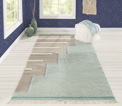 Long woven runner rug with beige stepped blocks on a soft blue base, fringed ends in a bright blue-walled room.