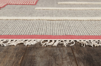 Beige striped woven rug with pink border and fringe tassels on a dark wooden floor.