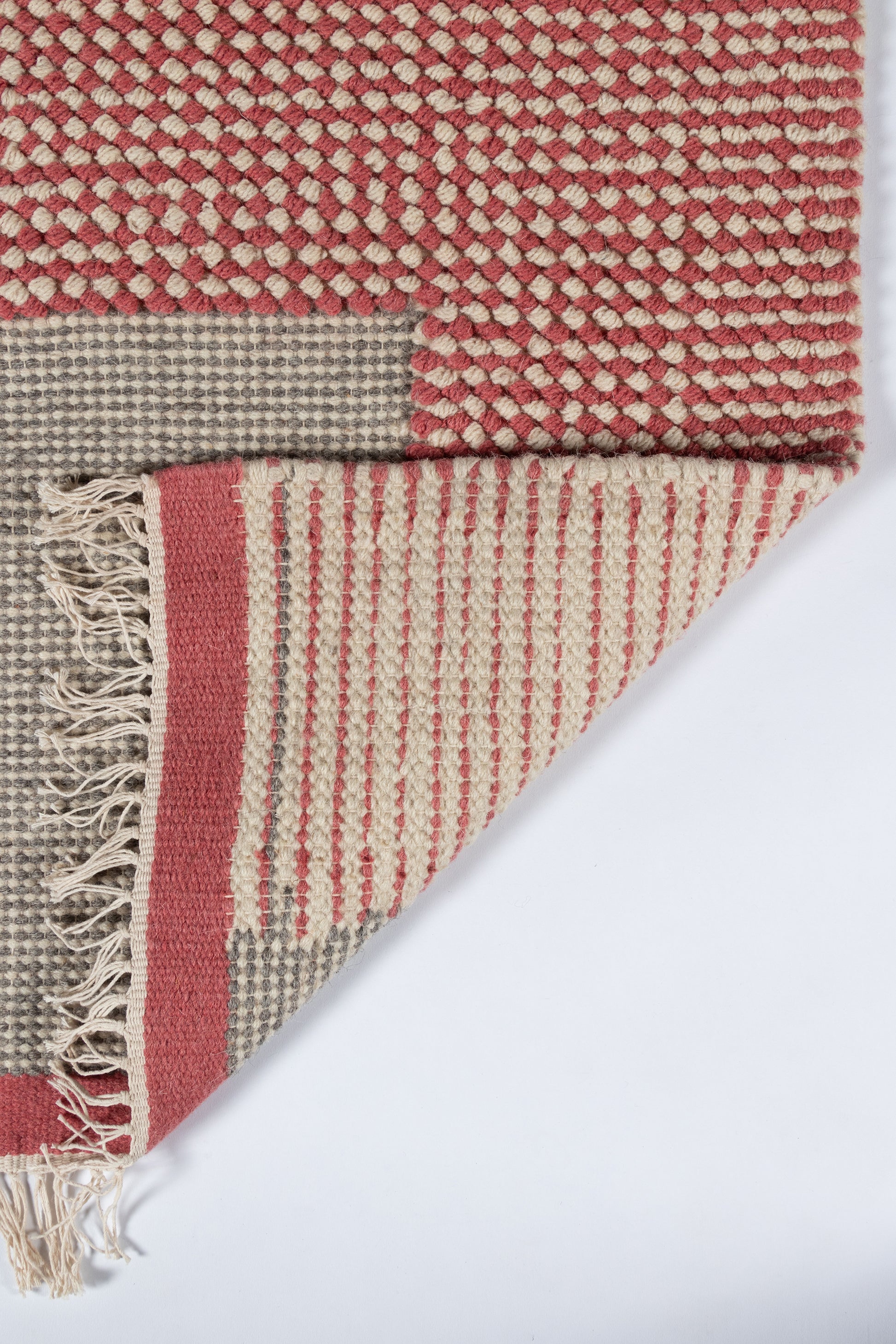 Red and cream woven rug with geometric texture, folded to reveal fringe and striped border.