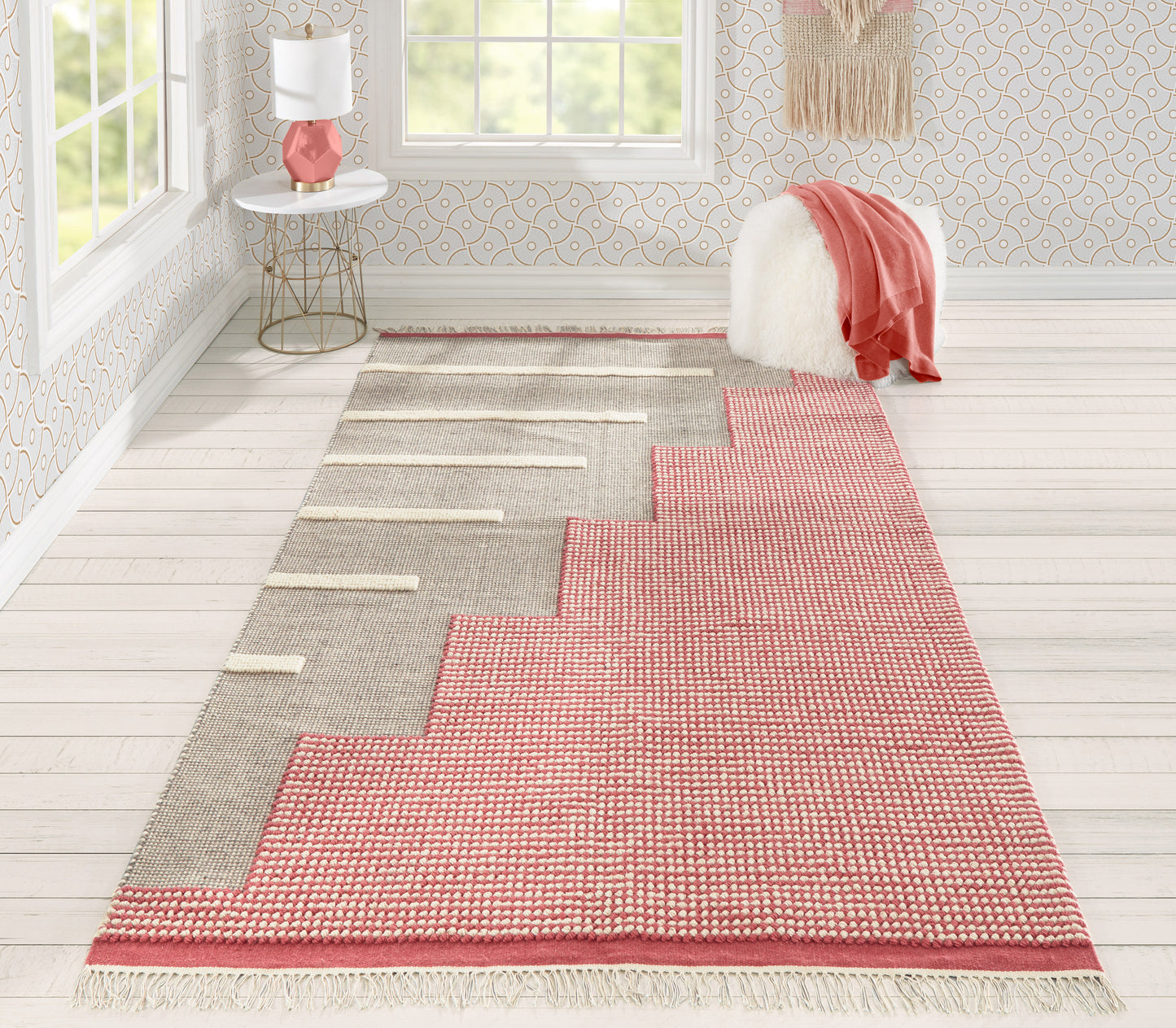 Pink and gray woven rug with stepped chevron motif and fringed ends in a bright modern room.