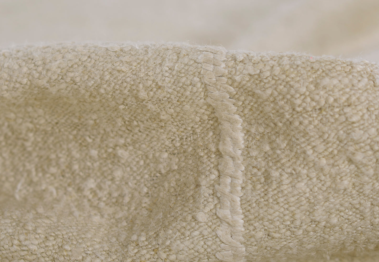 Ivory cream boucle fabric close-up with plush textured surface & stitched seam, cozy throw blanket edge detail.