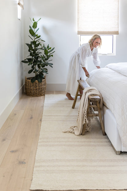 Long cream textured area rug in a neutral bedroom; woven pile with subtle stripes, complements light wood floor.