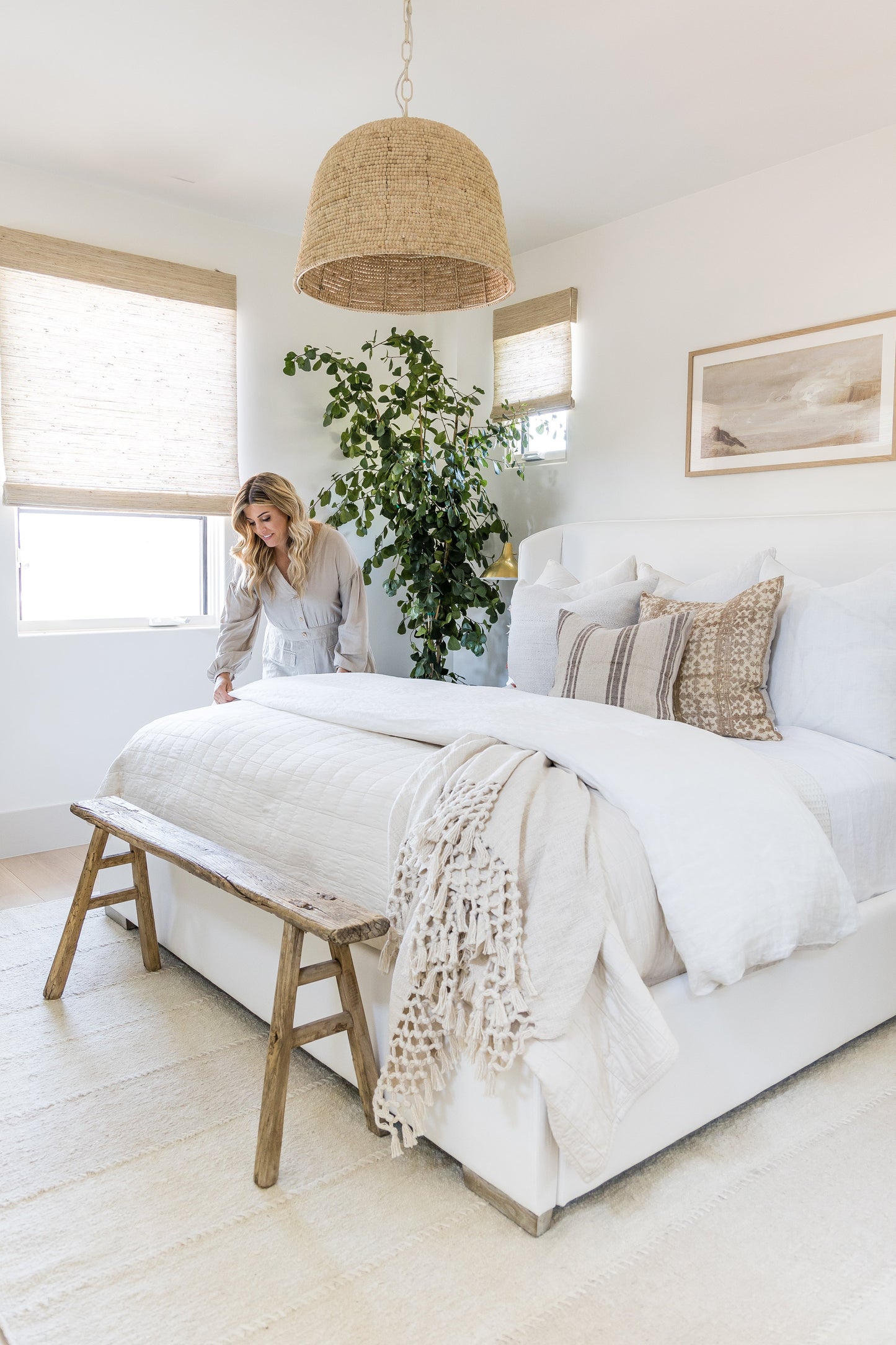 Neutral boho rug 10' x 14' in a bedroom scene with white linens, cream knit throw, rustic wooden bench, woven pendant light and a tall leafy plant.
