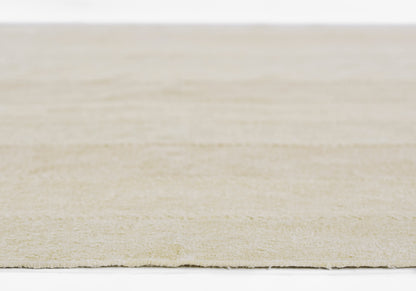 Beige textured rug with fringe edge on a white surface; soft neutral tones.
