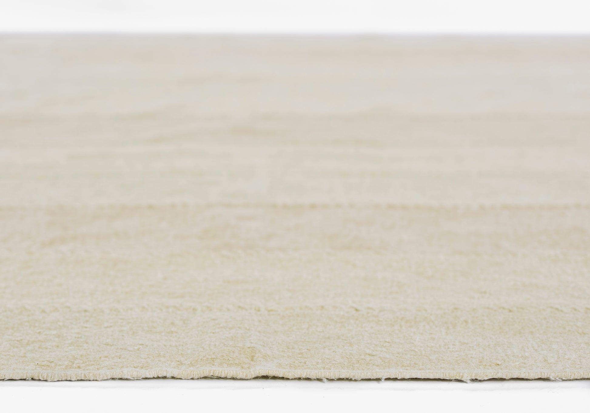 Beige textured rug close-up, soft wool-like pile with subtle fringe along edge.