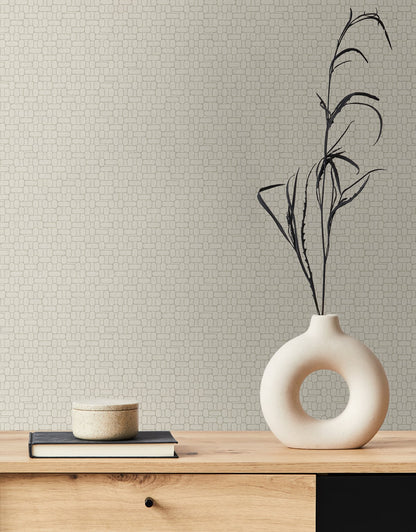 Round hollow ceramic vase with black branch stems on a light wood table, with stacked books and a beige dish.