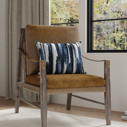 Tan leather lounge chair with weathered wood frame and leather strap arms, blue striped pillow by a window.