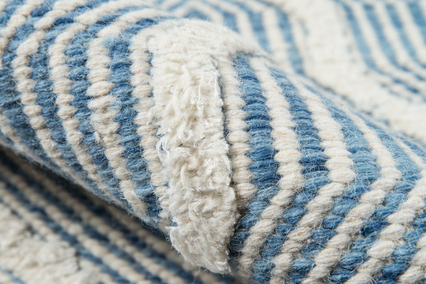 Close-up of blue and white striped woven rug with thick fibers and folded edge.