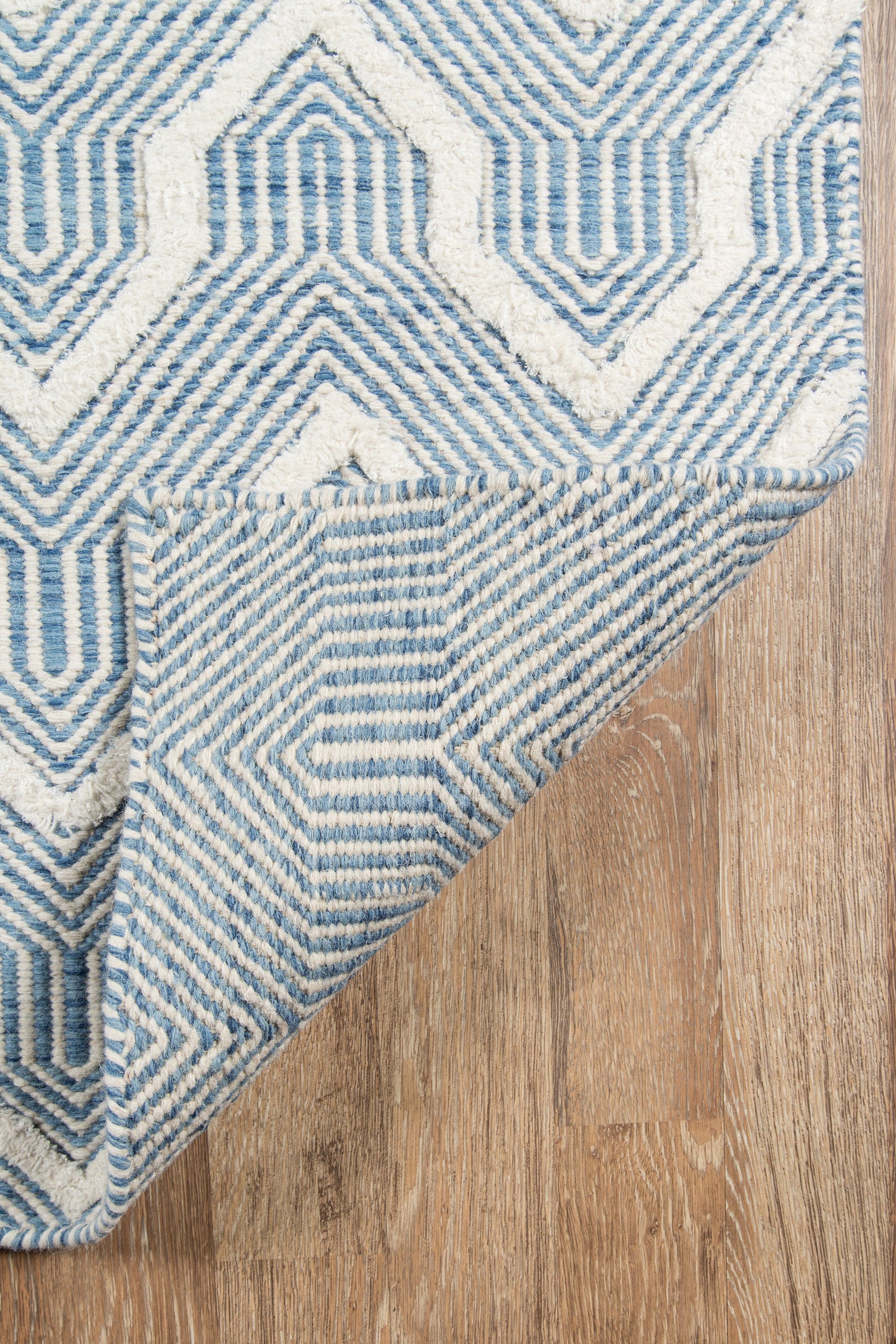 Blue-and-white geometric woven area rug with a diamond/maze pattern, folded corner on a wooden floor.
