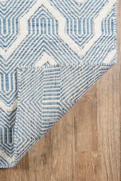 Blue and white geometric woven rug with maze pattern; folded corner reveals striped underside on wood floor.