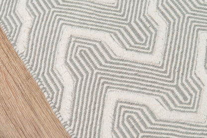 Gray and white geometric woven rug with raised maze pattern beside light wood floor.