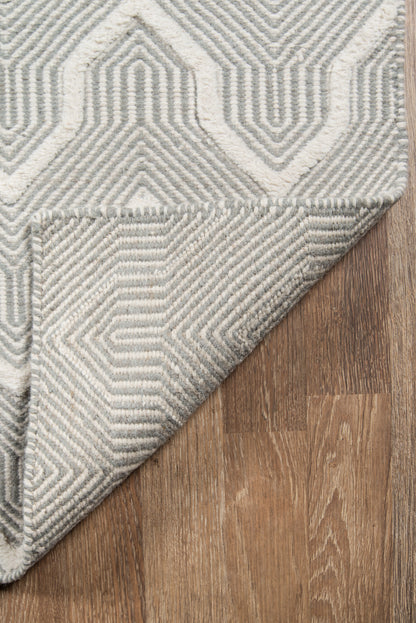 Gray and ivory geometric woven rug, textured pattern, folded corner on wood floor, modern living room style.