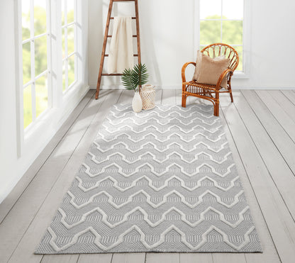Gray chevron area rug on light wooden flooring, with wicker chair, wooden ladder, and potted plant.