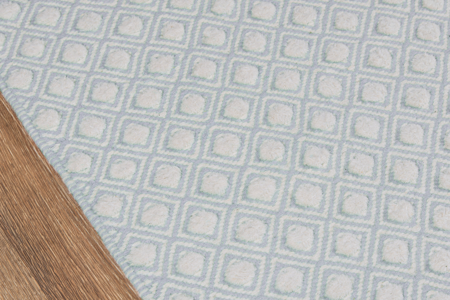 Blue woven rug with white square-grid pattern; geometric, textured motif on wooden floor.