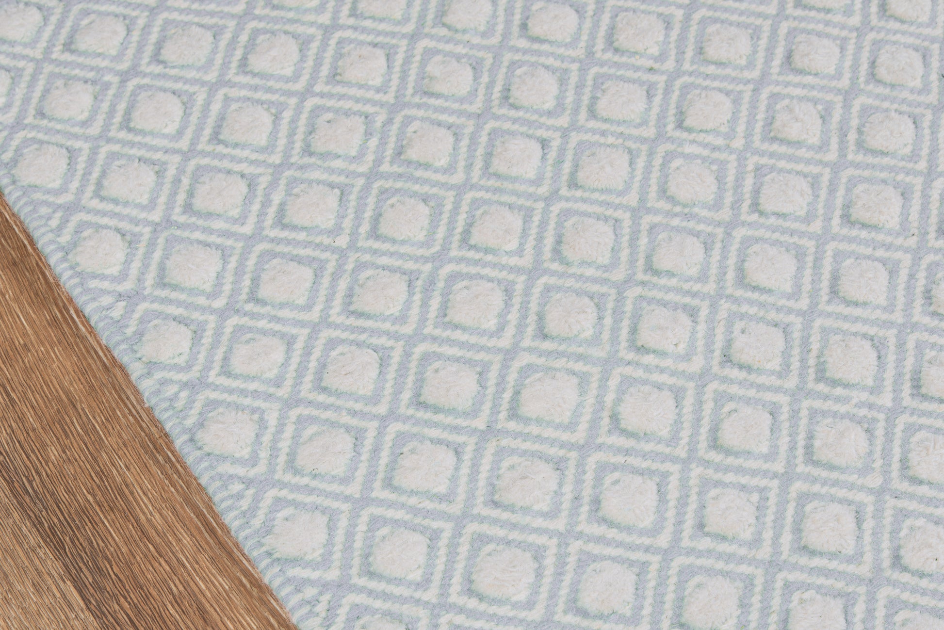 Blue woven rug with white square-grid pattern; geometric, textured motif on wooden floor.
