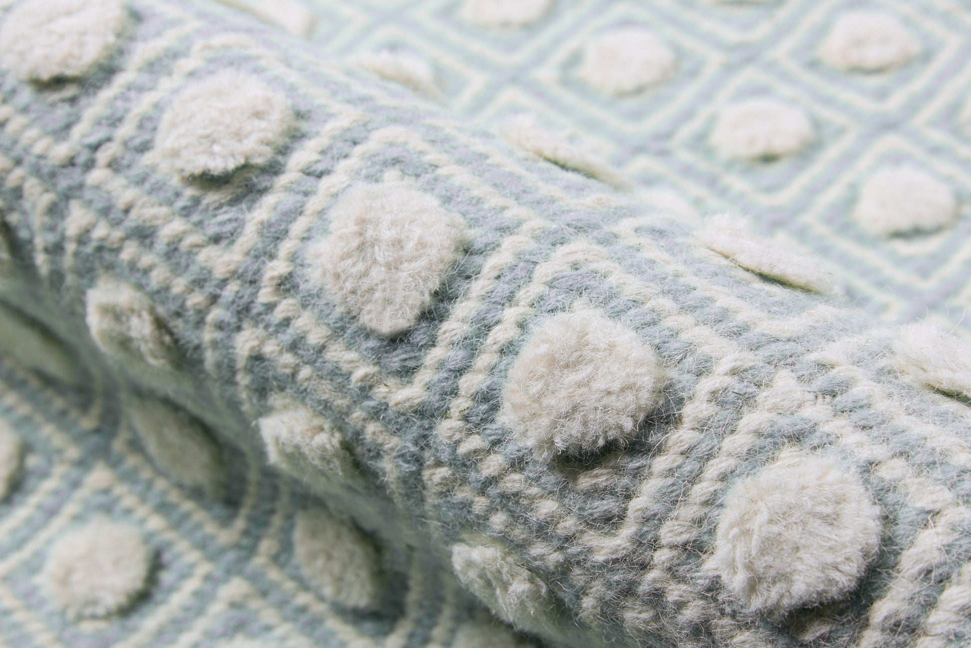 Soft blue knit throw with cream pom-pom bobbles and geometric pattern, fuzzy texture.