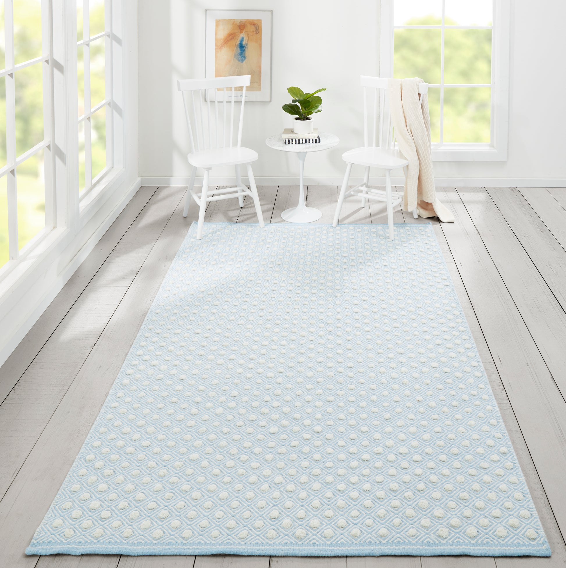 Light blue rug with white raised dot pattern between two white chairs and a small round table in a bright sunlit room.