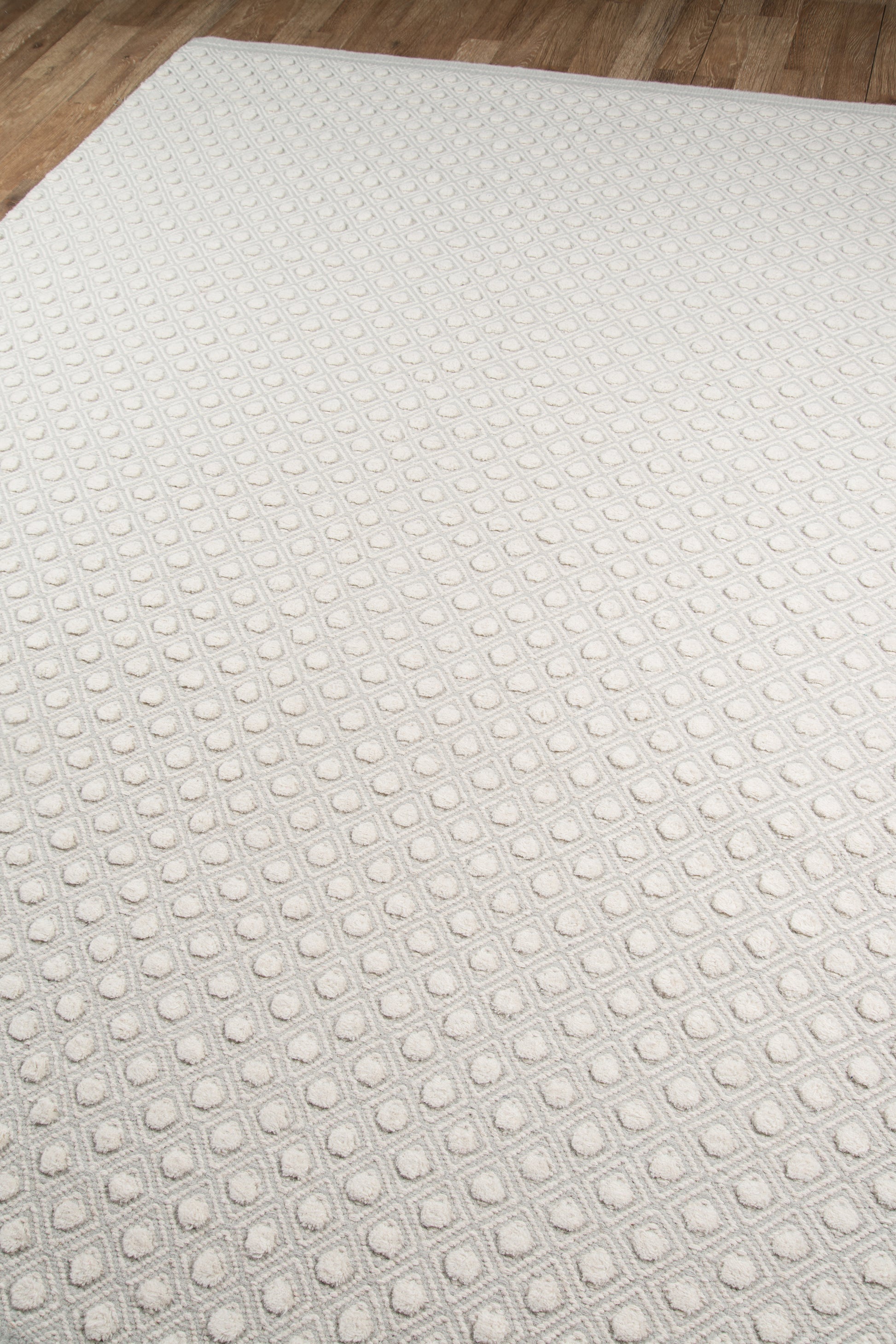 Light gray rug with a raised rounded-square grid pattern on a wood floor.