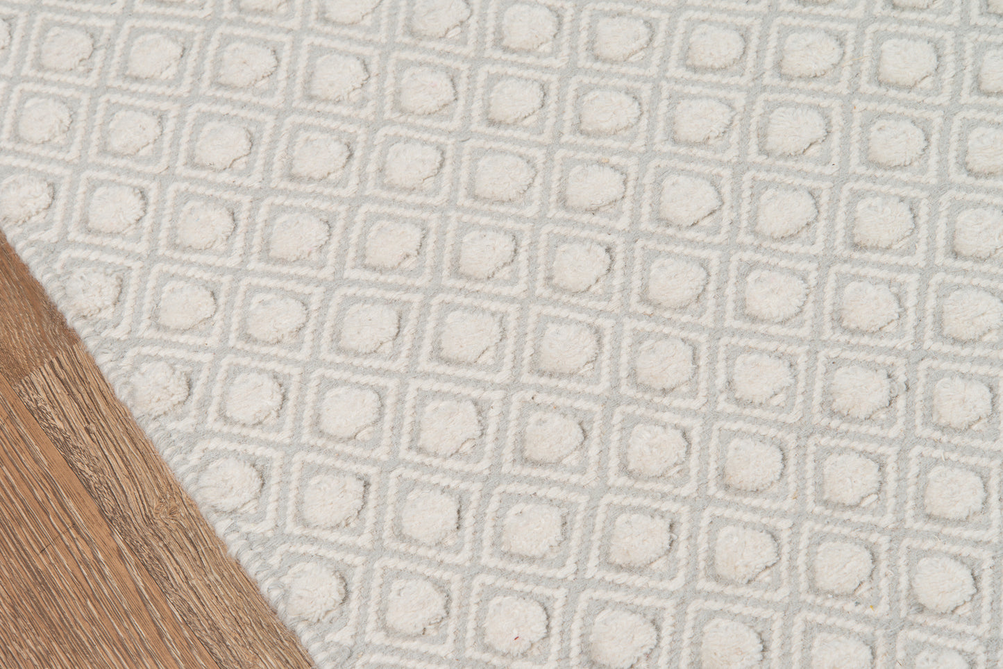 Grey and off-white geometric rug with raised square tufting on light wood floor.