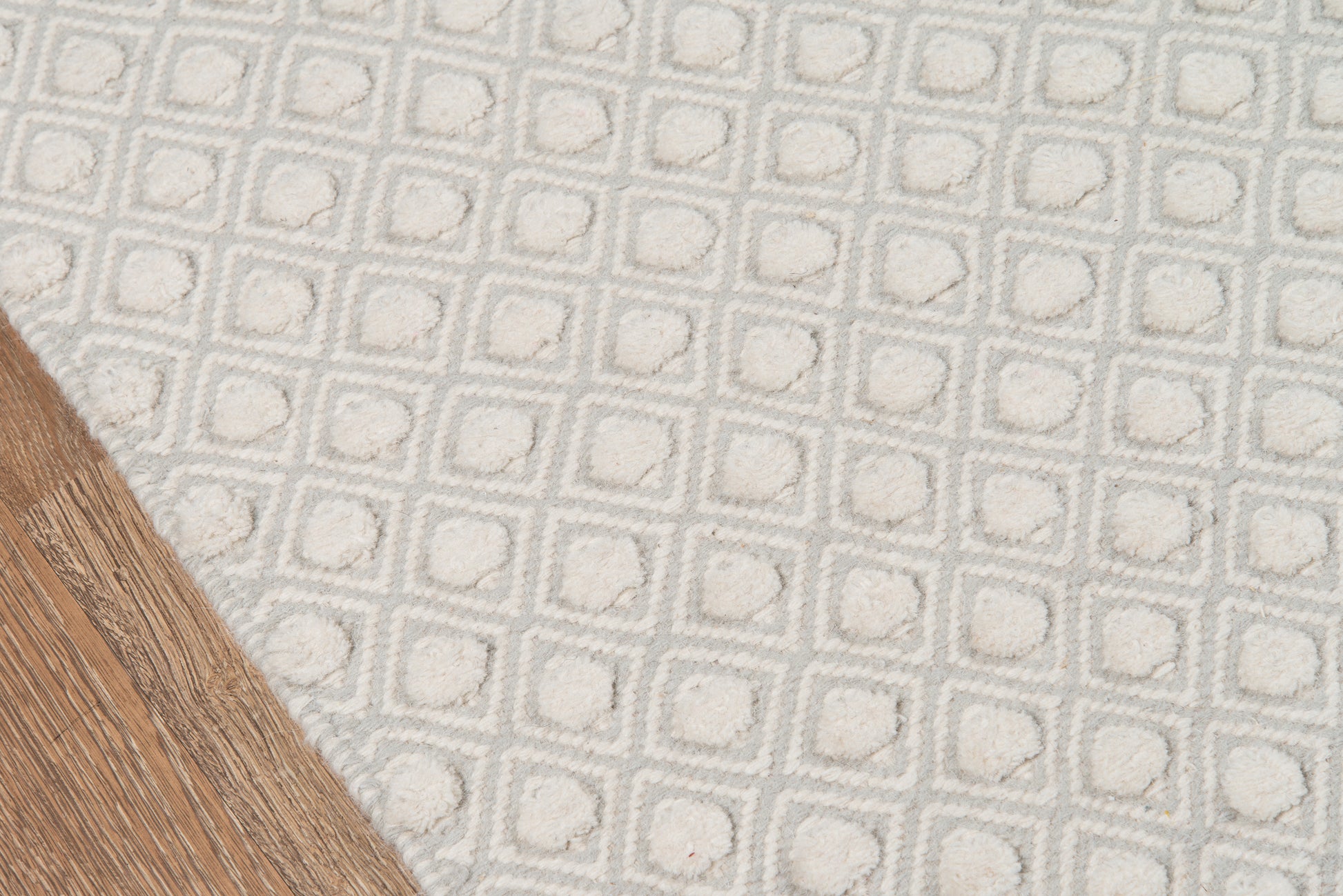 Gray tufted rug featuring a square grid pattern on a light backdrop, laid on a wooden floor.